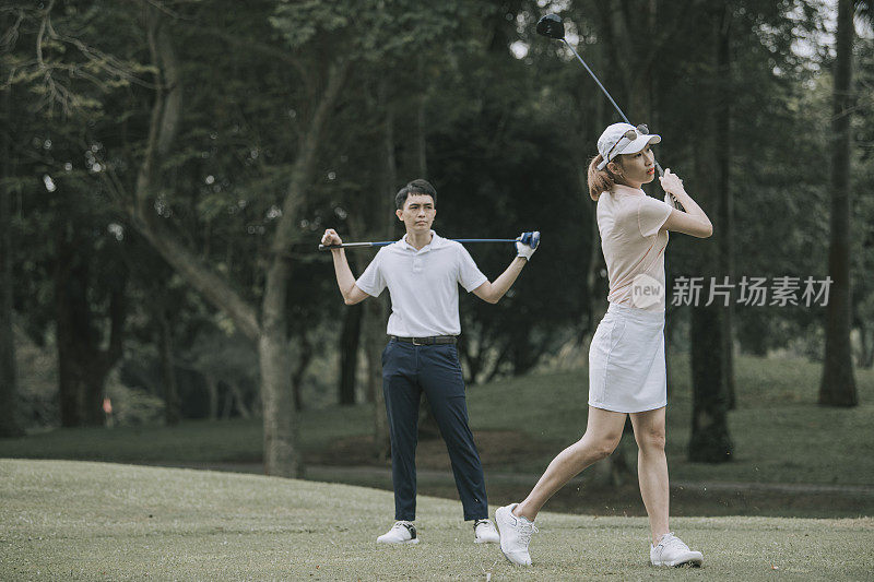 asian chinese female golfer teeing off at golf course with her husband beside